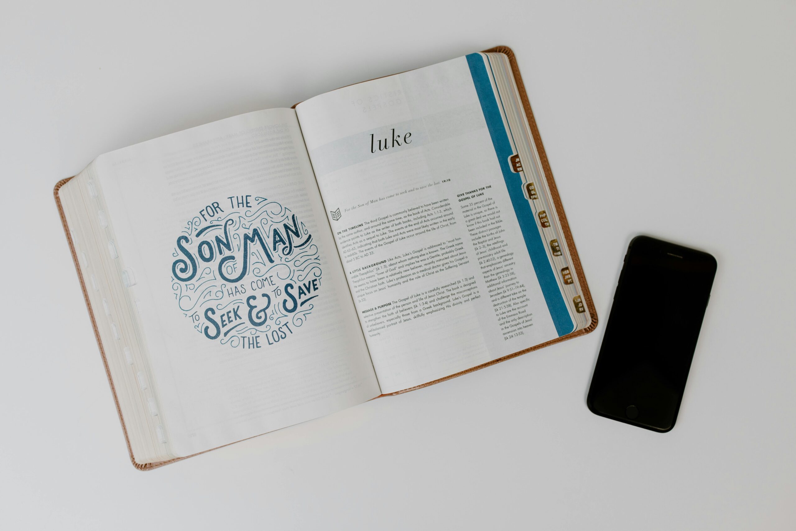 pexels-photo-8383416-8383416 Open Bible displaying the Book of Luke next to a smartphone on a white surface.